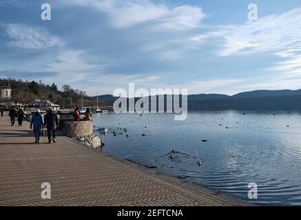 Viverone lake, Italy - february 2021: people stroll along the pier of an alpine lake on a spring day Stock Photo