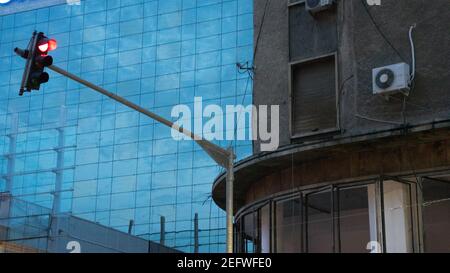 Bucharest, Romania. Hanging red traffic light against the blue glass modern office building beside the old building Stock Photo