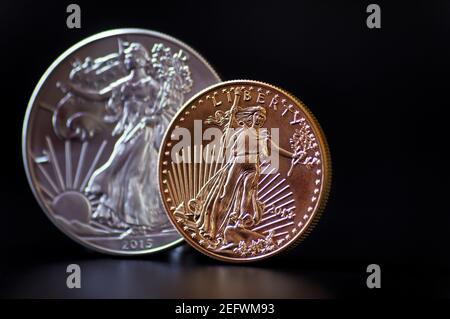 An in focus one ounce gold coin with an out of focus American silver Eagle coin behind it, on a black background Stock Photo
