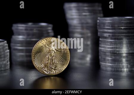 A one ounce gold coin in front stacks of 1 ounce American silver Eagle coins Stock Photo