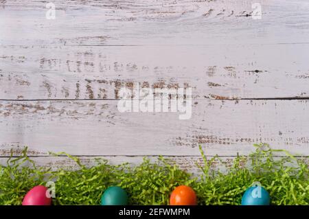 Four colorful painted easter eggs on bottom of frame on top of easter grass, with white wooden background and copy space Stock Photo