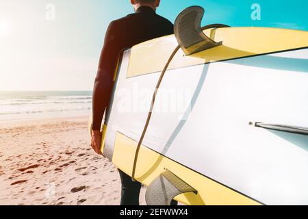 Surfer in wetsuit holding yellow surfboard on the beach near the ocean Stock Photo