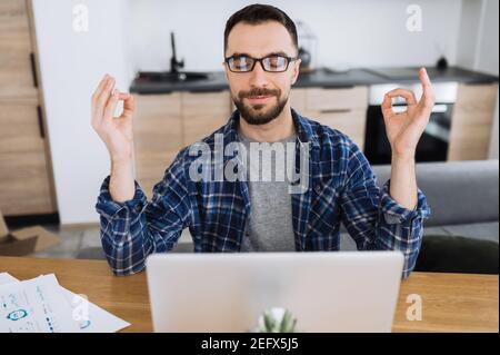 Successful male freelancer working from home office. Confident young entrepreneur sits at the desk, meditate, charging by good energy, calm down, through out negative emotions, taking break from work Stock Photo