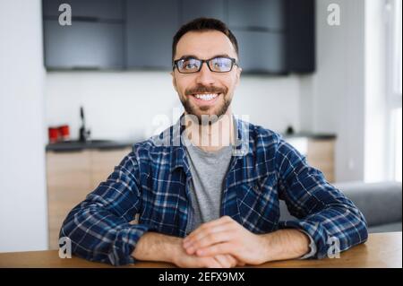 Webcam portrait of happy freelancer guy during video conference, he looks at the camera and smiling. Young adult stylish intelligent man wearing eyeglasses distantly works from home Stock Photo