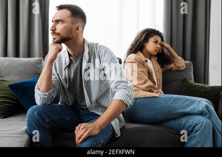 Smiling multiracial black curly girl uses cell phone, talking with friends or family while sits on the couch at living room and looks at camera, communication concept Stock Photo