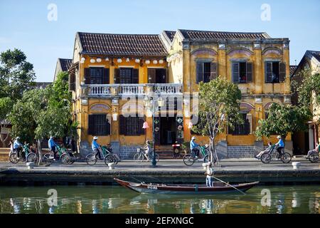 Fleets of trishaw drivers carry tourists past old buildings on the banks of the Thu Bon River along Bach Dang Road, Hoi An, Vietnam Stock Photo