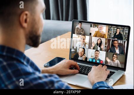 Over shoulder view to a laptop screen with many multiracial successful employees, coworkers communicating by video call, online meeting concept. Video conference with many people together Stock Photo