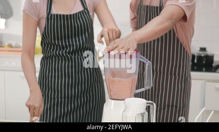 Happy young family couple husband and wife making fresh apple smoothie in kitchen together. The man and woman help each blender the apples with a juic Stock Photo