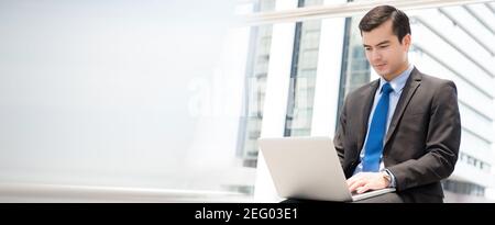 Businessman using laptop computer while sitting outdoor in the city, panoramic banner with copy space Stock Photo