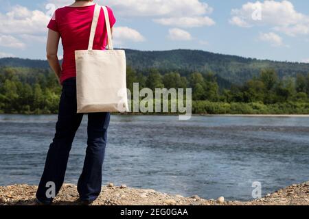 Woman in red t-shirt carrying empty reusable shopping bag mockup. Female hand holding canvas eco friendly tote bag mock up Stock Photo