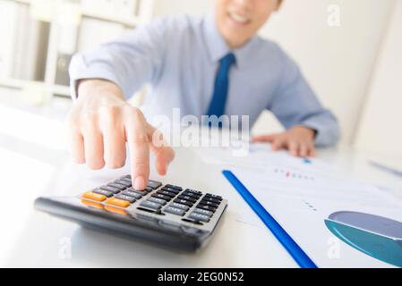 Businessman pressing calculator button at working table in the office - financial analyzing concept Stock Photo