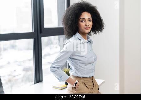 Portrait of a self made leader confident young mixed-race female entrepreneur businesswoman with Afro hairstyle in casual clothes standing with hands Stock Photo