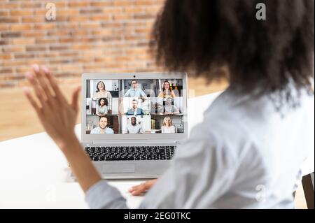 A close-up of mixed-race woman waving at the laptop screen with people profiles, using an application for distance video communication with coworkers Stock Photo