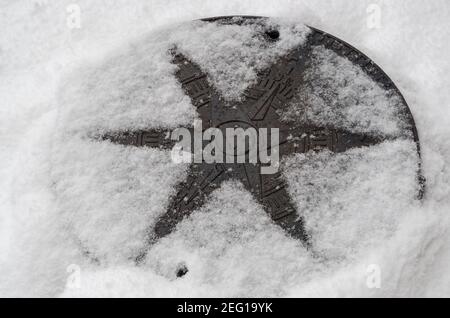 Metal hatch of heating main well with image of wind rose on lid, dusted with snow. On surface thawed outline of six-pointed star and holes of vents. Stock Photo