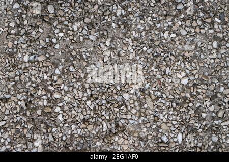 Background formed by the lower part of the facade of the building, a fragment of the wall with inclusions of gray stone pebbles in black asphalt and d Stock Photo