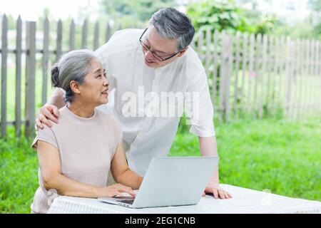 Happy old couple use computer to surf in the park Stock Photo