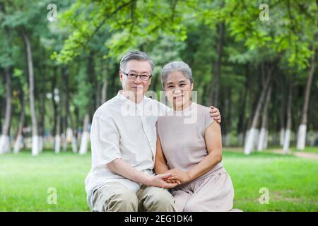Happy old couple sitting on the park chair arms around shoulders Stock Photo