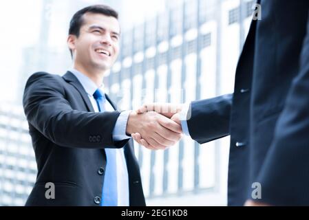 Businessmen making handshake in front of office buildings in the city - greeting, dealing, merger and acquisition concepts Stock Photo