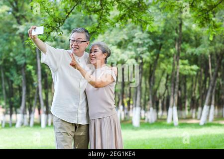 Happy old couple take selfie with mobile phone in the park  Stock Photo
