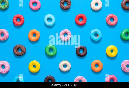 Flat lay with multicolored glazed doughnuts isolated on a blue background. Homemade chocolate doughnuts in different colors and styles. Stock Photo