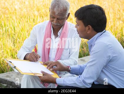 Selective focus on farmer, Banker or corporate officer getting sign from farmer while sitting near the farmland - concept of contract farming Stock Photo