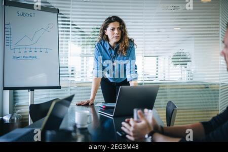 Female professional leaning to conference table and listening to a colleagues suggestion. businesswoman discussing with male colleague during budget p Stock Photo