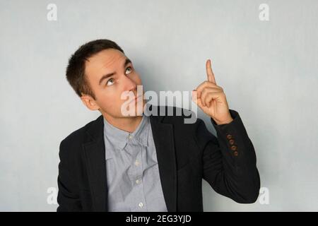 businessman points up with a thoughtful expression on blue background. Cute young man gives a presentation. Copy space. Copyspace. Stock Photo