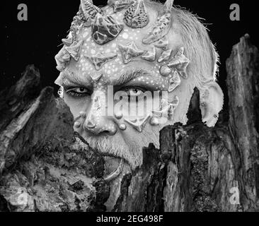Devil. Tree spirit and fantasy concept. Monster with sharp thorns and warts. Druid behind old bark on black background. Man with dragon skin and Stock Photo
