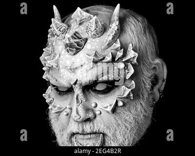Devil with dragon skin and grey beard. Evil monster with sharp thorns and warts on face. Horror and fantasy concept. Demon head on black background. Stock Photo