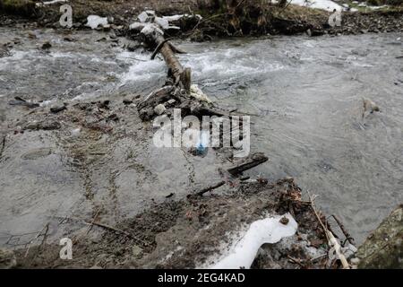 Plastic bottle on a running mountain stream during a cold and sunny winter day in the Romanian Carpathian Mountains. Stock Photo