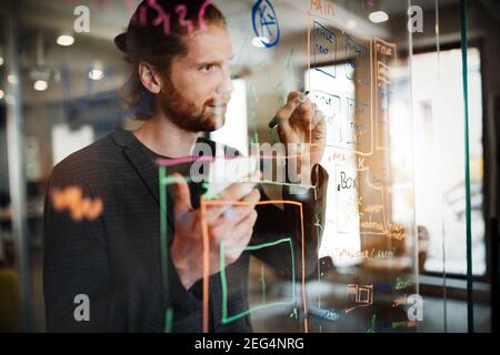 Handsome man working and writing on glass board in office. Business, technology, research concept Stock Photo