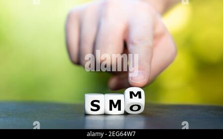 Hand turns dice and changes the abbreviation SMO (social media marketing) to SMM (social media optimization). Stock Photo