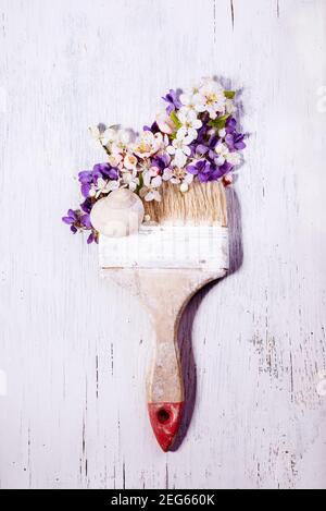 Vintage dirty paintbrush drawing with beautiful first spring flowers, violets, and cherry tree blossom on a white rustic wooden table. Stock Photo