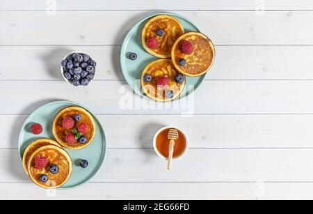 Two plates with tasty american pancakes with raspberries, blueberries, and honey. Top view, marble table. Stock Photo