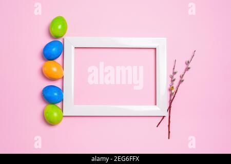 easter holiday willow branches and colorful painted eggs photo frame on a pastel pink background. composition easter. Stock Photo