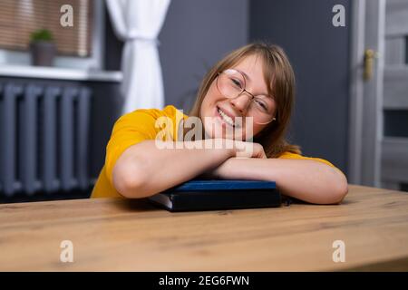 A young student, she smiles nicely, dreaming of a spectacular career success, sitting at a wooden table in her home office. The concept of receiving Stock Photo