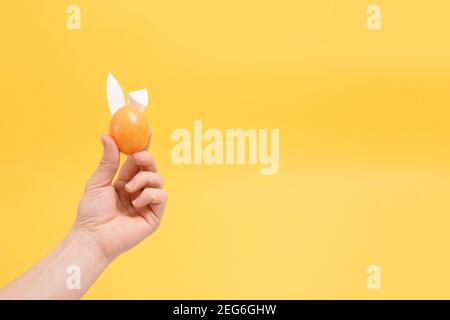 painted colorful eggs in hand with rabbit ears for easter holiday yellow background. background for the poster, place for the text. Stock Photo