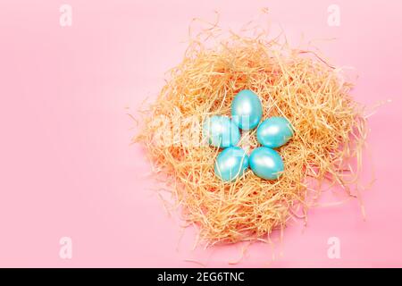 Happy easter simple background, colored pearl blue eggs in hay nest over bright pink color, top view with copy space Stock Photo
