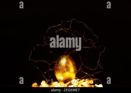 Easter golden egg in gold decorations with lights over dark background, magic of easter concept Stock Photo