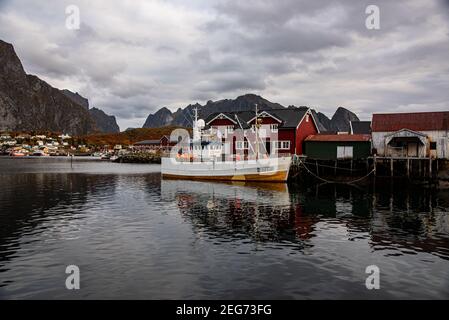 Typical Norwegian fishing village with traditional red rorbu huts, Reine, Lofoten Islands, Norway - fischer mole for boats in the background - the eve