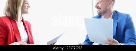 Man in blue jacket and woman in red jacket hold contract and cup and look at each other. Stock Photo