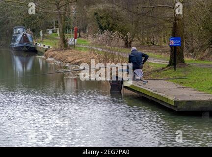 Melbourne, East Yorkshire, England, 17-02-2021 - a man fishing from the towpath of Pocklington Canal with narrow boat in the background. Stock Photo