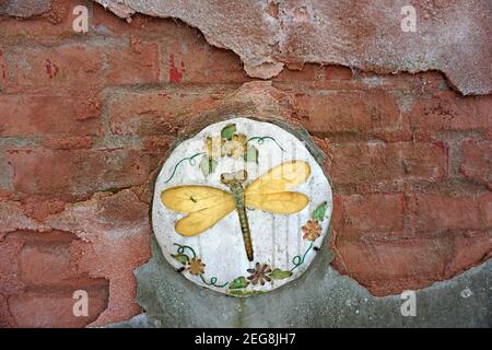 A special wall. Old bricks, the red and grey plaster half-crumbled with an old round tile with a gold colored dragonfly Stock Photo