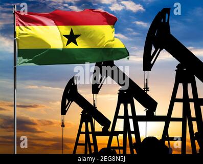 Oil rigs against the backdrop of the colorful sky and a flagpole with the flag of Ghana. The concept of oil production, minerals, development of new d Stock Photo