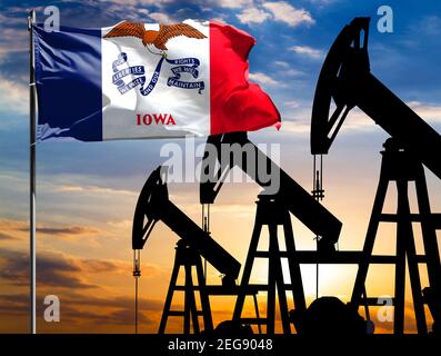 Oil rigs against the backdrop of the colorful sky and a flagpole with the flag State of Iowa. The concept of oil production, minerals, development of Stock Photo