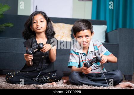 Two kids busy playing video game using joystick at home while sitting on floor - concept of kids game addiction and leisure and weekend activity and Stock Photo