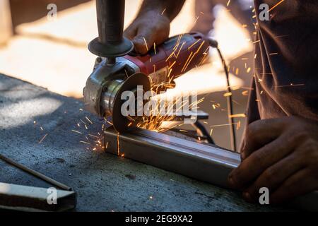 a man working cutting metal bar with a circular electric tool that shoots sparks Stock Photo