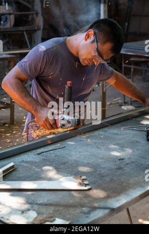 a man working cutting metal bar with a circular electric tool that shoots sparks Stock Photo