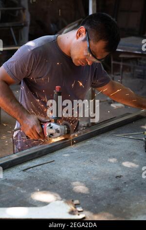 a man working cutting metal bar with a circular electric tool that shoots sparks Stock Photo