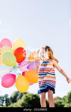 Happy girl running in the park with a bunch of colorful balloons. Childhood fun. Stock Photo